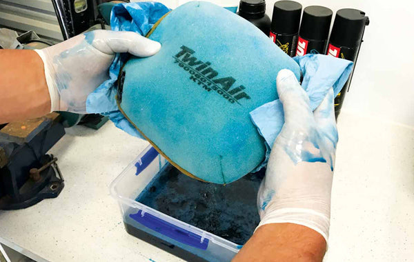 POV holding a clean and freshly oiled air filter. Wearing gloves to prevent getting the harsh chemicals on their skin during the cleaning process.